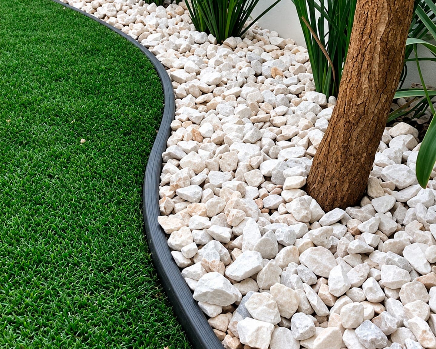 Jardinera con piedra decorativa blanca junto a pasto sintético