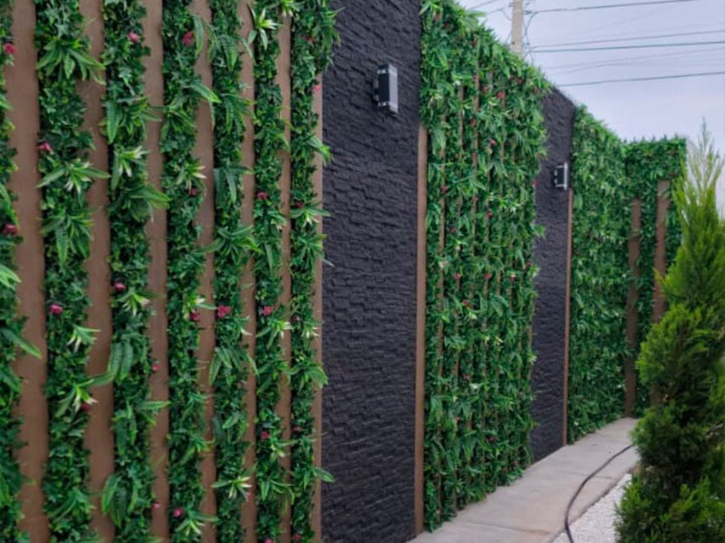 Muro decorativo con franjas de follaje sintético y paneles de piedra negra