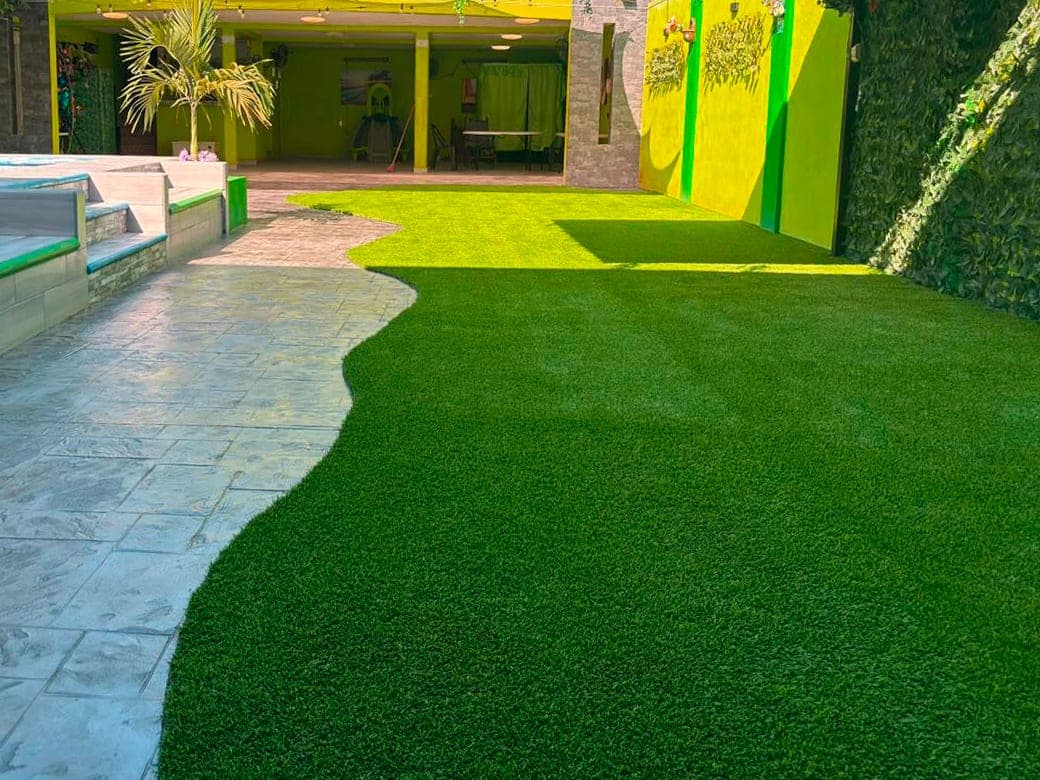 Patio con pasto sintético en curva junto a un camino de concreto estampado