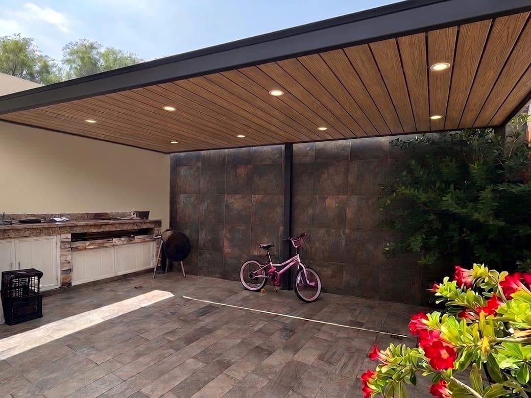 Pérgola con plafón de madera e iluminación empotrada sobre un patio con asador
