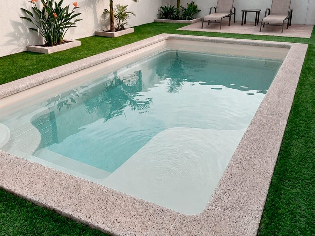 Piscina de fibra de vidrio con borde de granito y pasto sintético alrededor