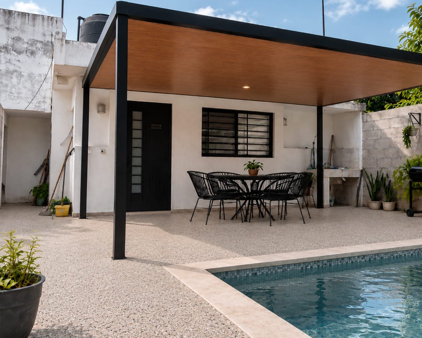 Pérgola con plafón de madera sobre un patio de granito granulado junto a la piscina