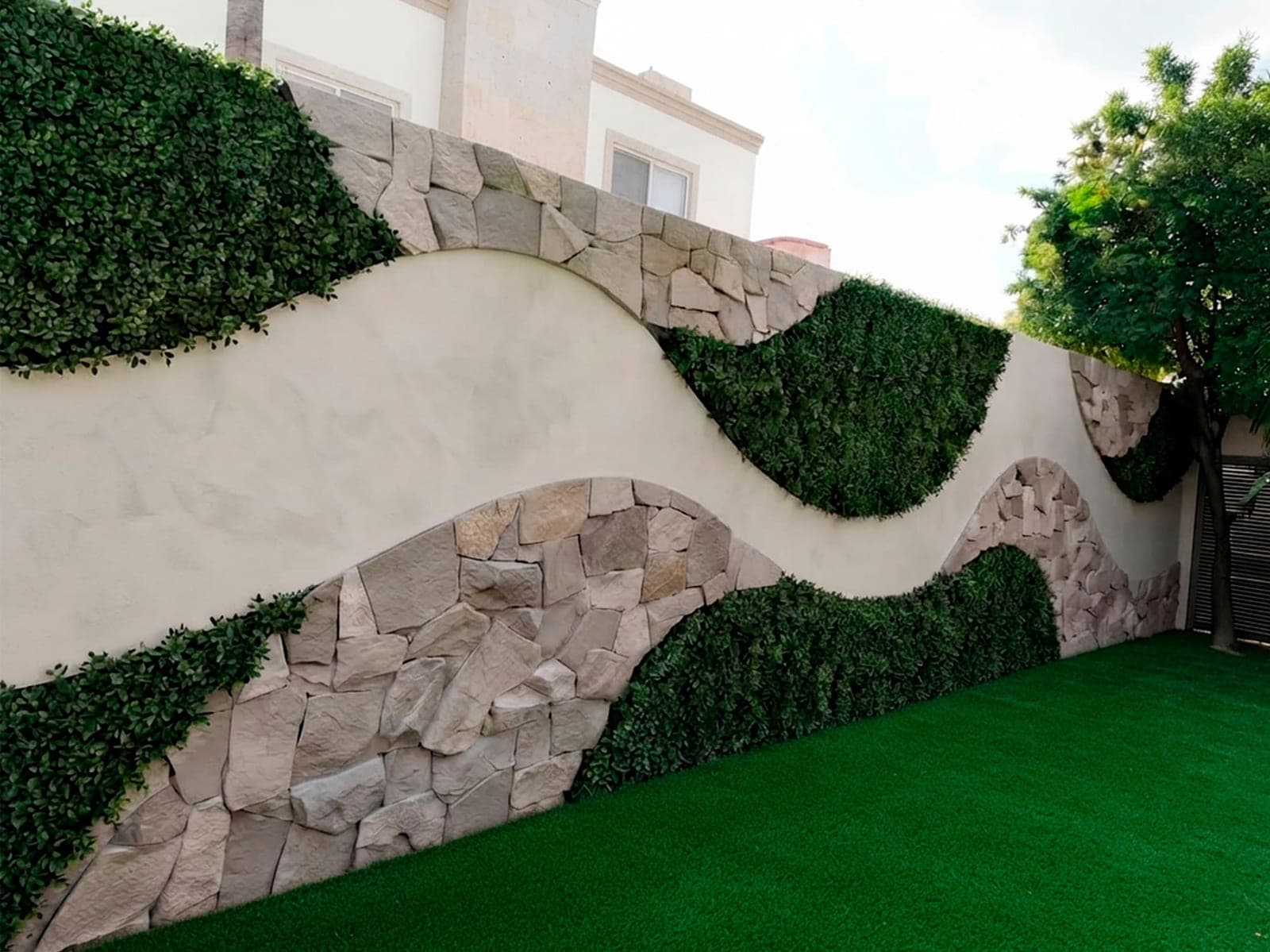 La misma barda terminada con muro de piedra natural en curva y follaje sintético