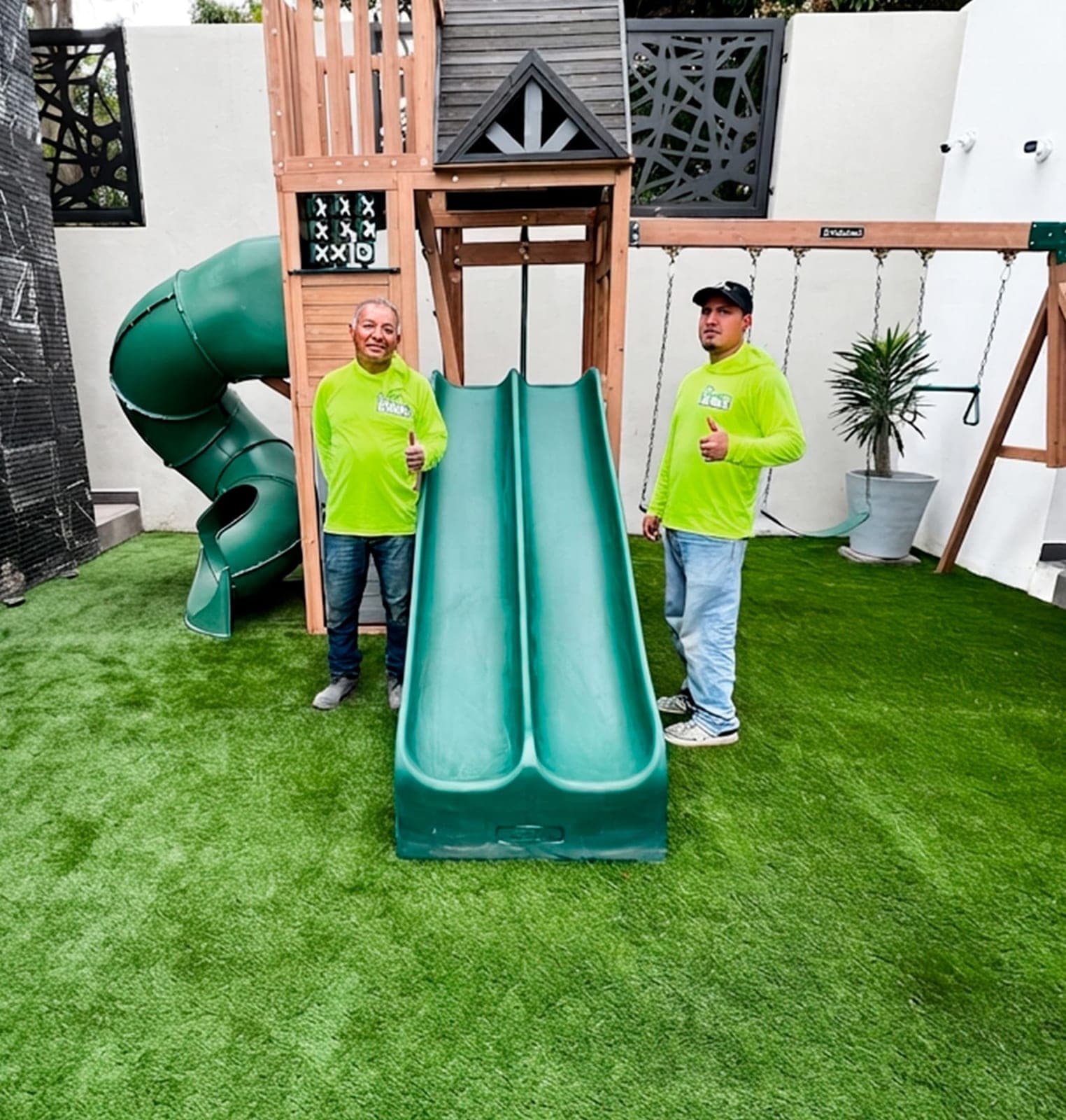 Dos instaladores de Mr. Patio en un patio terminado con pasto sintético y juegos infantiles