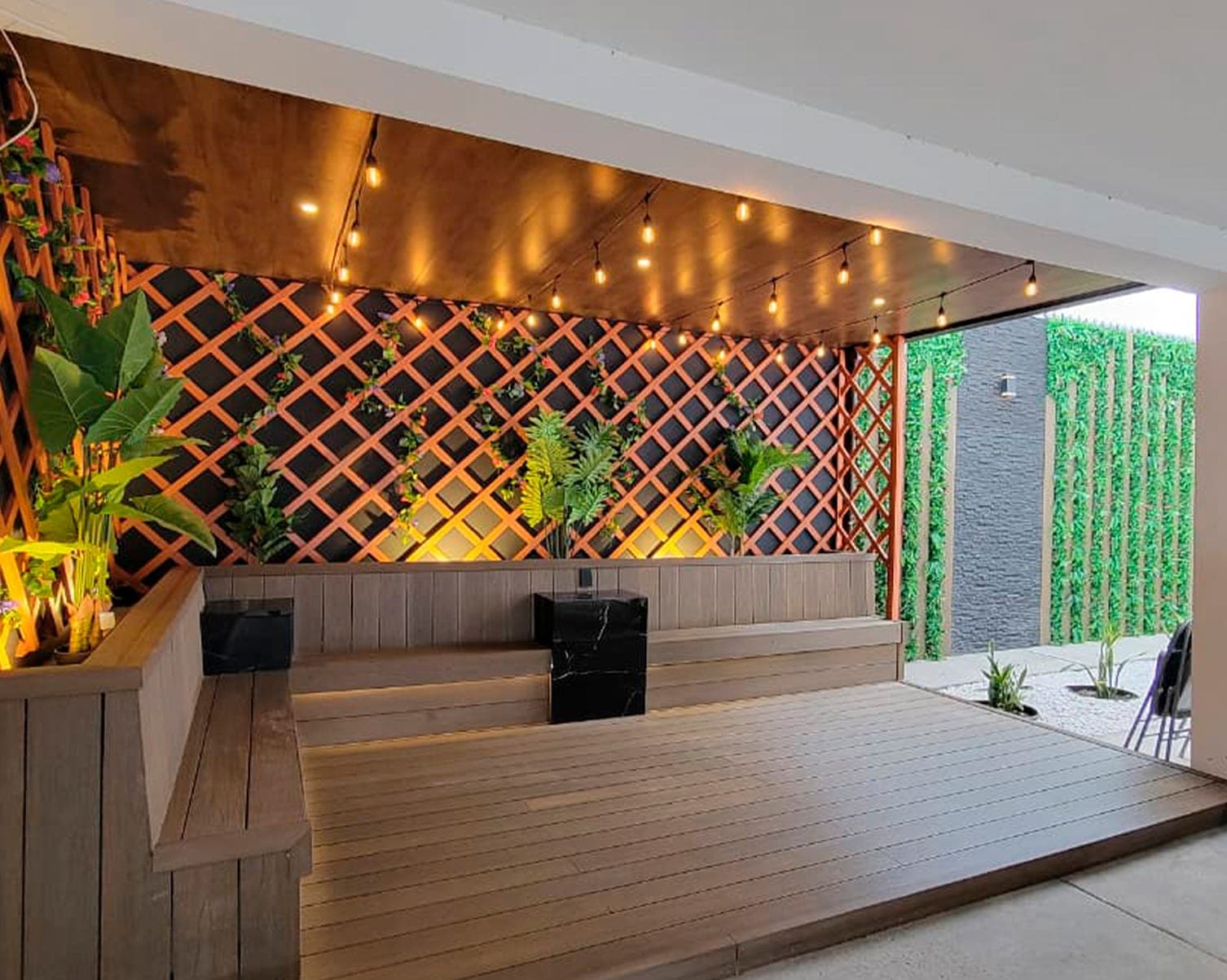 Terraza techada con deck de madera, celosía iluminada y jardín vertical, terminada por Mr. Patio