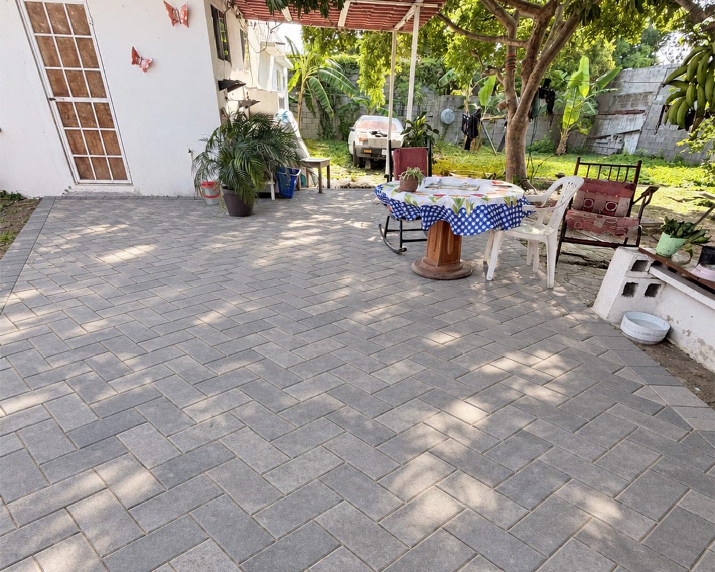 Patio con piso de adoquín gris, mesa y sillas de jardín