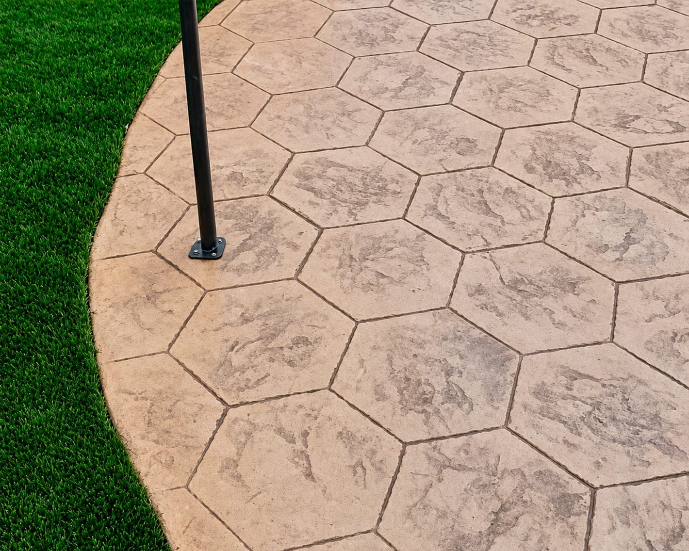 Concreto estampado con diseño hexagonal junto a un área de pasto sintético
