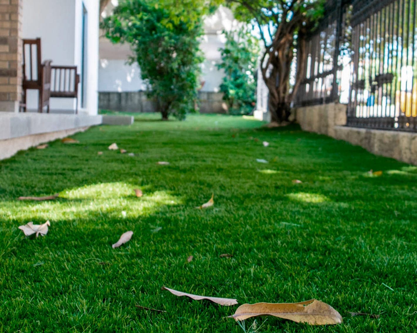 Jardín residencial con pasto sintético y reja metálica al fondo
