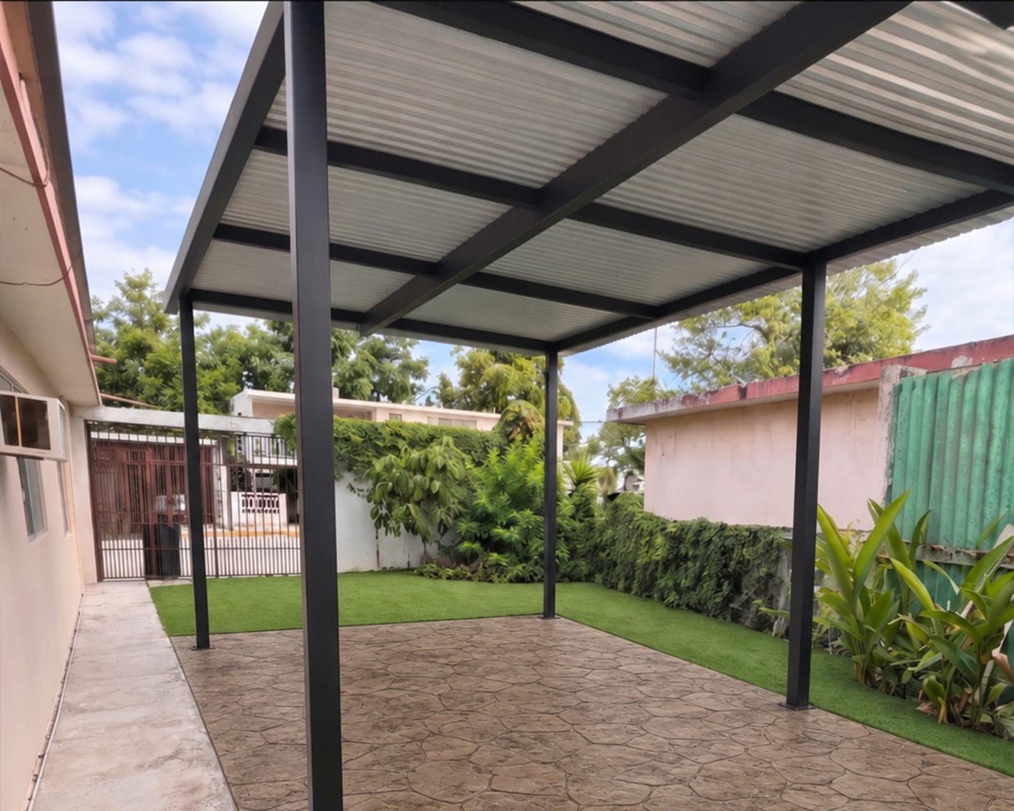 Pérgola metálica con techo de lámina sobre un patio con pasto sintético