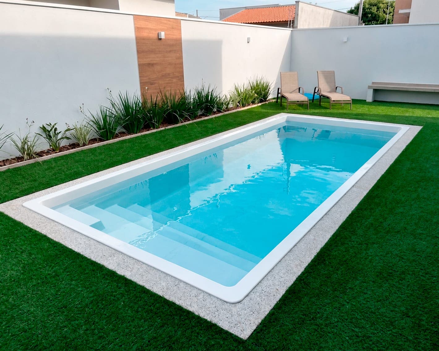 Piscina rectangular de fibra de vidrio rodeada de pasto sintético y camastros
