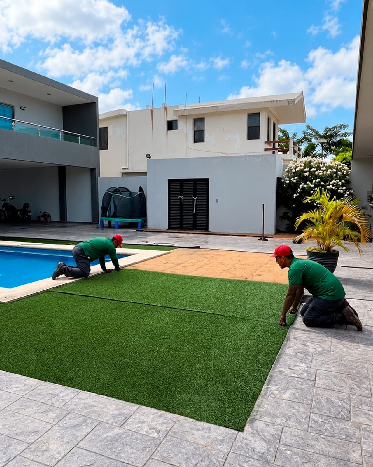 Dos instaladores colocando pasto sintético junto a una piscina