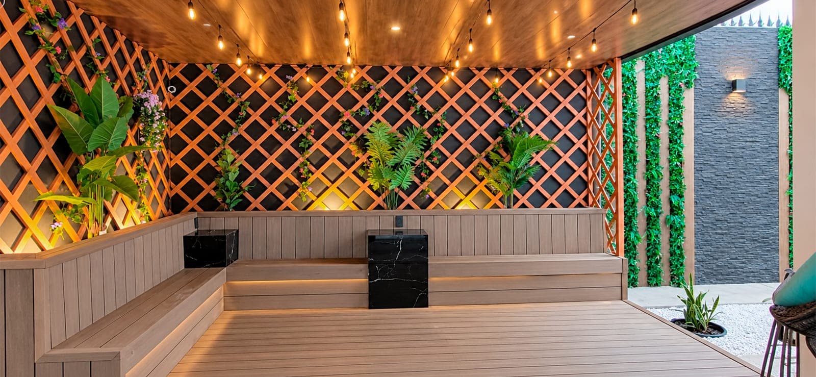 Terraza con deck, bancas empotradas, celosía de madera iluminada y muro de follaje sintético